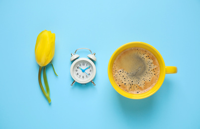 Photo of Delicious morning coffee, alarm clock and tulip on light blue background, flat lay