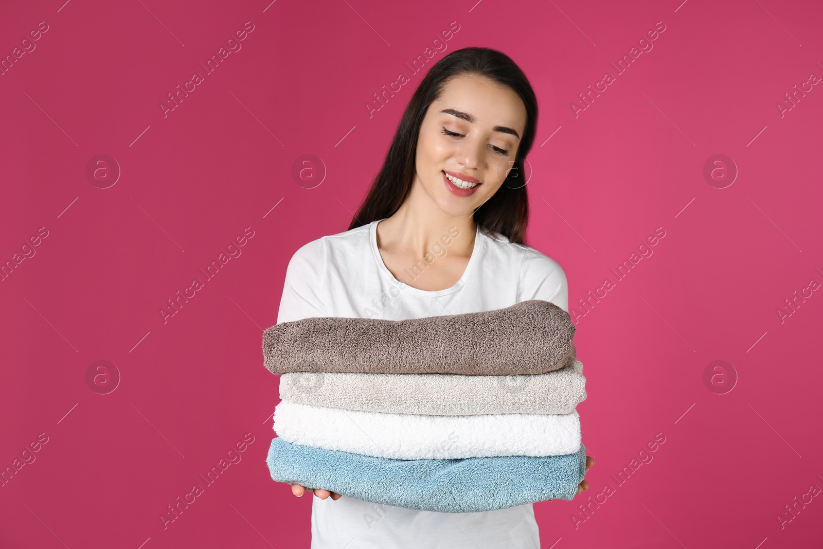 Photo of Happy young woman holding clean towels on color background. Laundry day