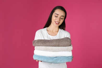 Photo of Happy young woman holding clean towels on color background. Laundry day