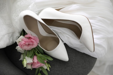 Photo of Pair of white high heel shoes, flowers and wedding dress on chair
