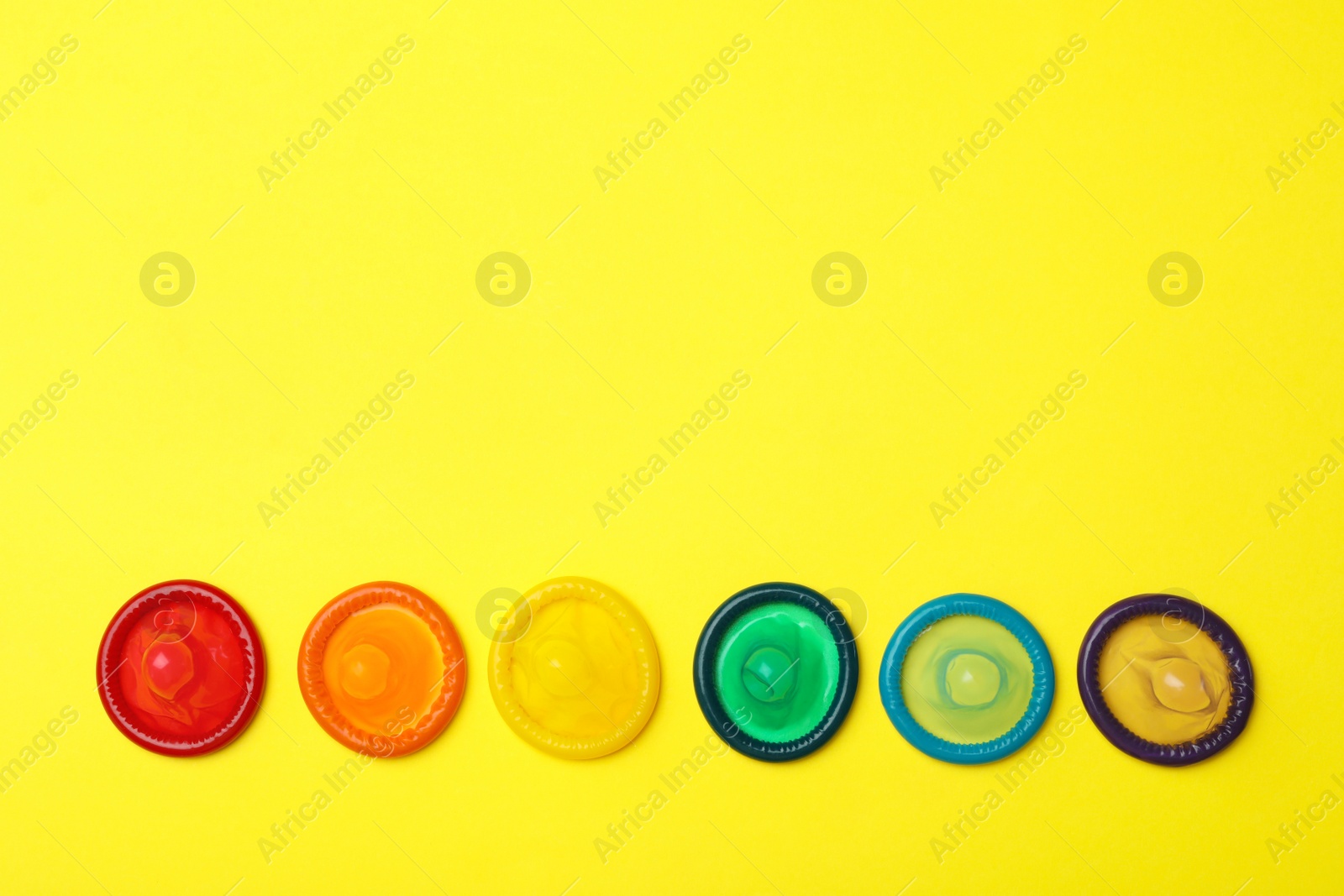 Photo of Flat lay composition with colorful condoms on yellow background, space for text. LGBT concept