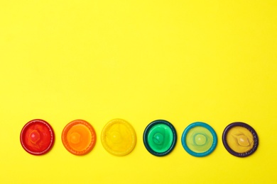 Flat lay composition with colorful condoms on yellow background, space for text. LGBT concept