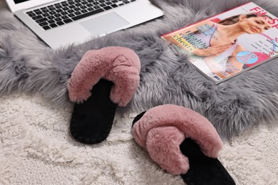 Soft slippers, magazine and laptop on carpet, closeup