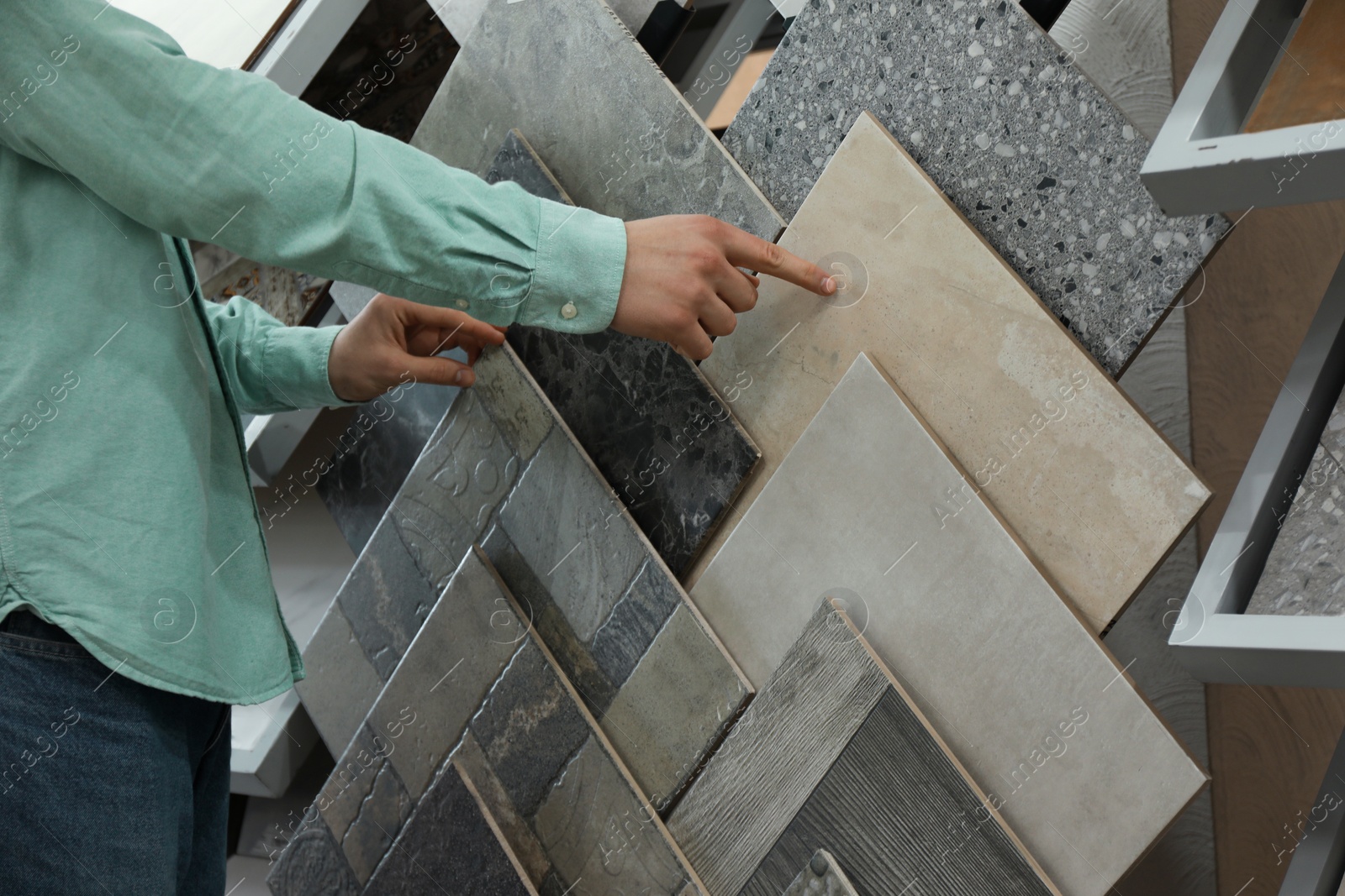 Photo of Man choosing tile among different samples in store, closeup