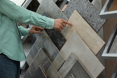 Photo of Man choosing tile among different samples in store, closeup