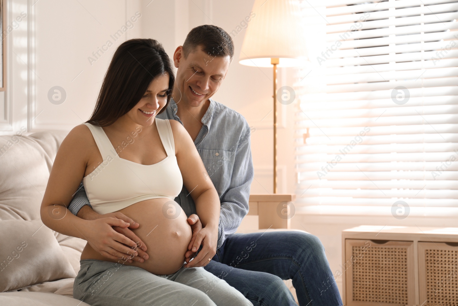 Photo of Man touching his pregnant wife's belly at home. Space for text