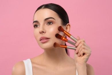 Beautiful woman with different makeup brushes on pink background