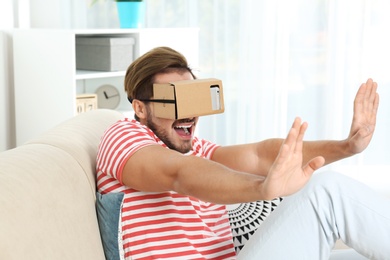 Photo of Young man using cardboard virtual reality headset at home