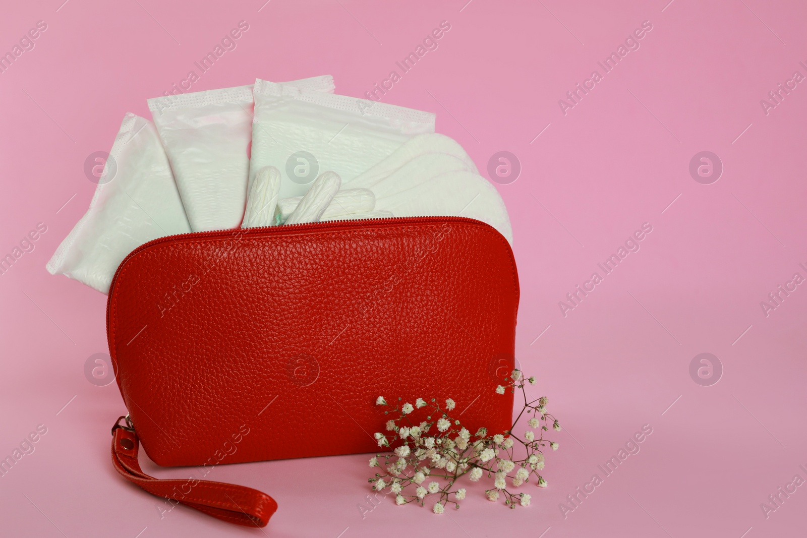 Photo of Menstrual pads, pantyliners and tampons in bag near flowers on pink background