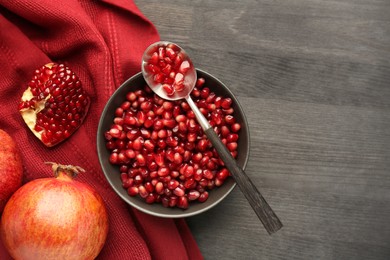 Photo of Tasty ripe pomegranates and grains on dark wooden table, flat lay. Space for text