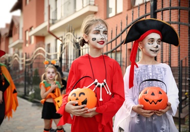 Photo of Cute little kids with pumpkin candy buckets wearing Halloween costumes going trick-or-treating outdoors