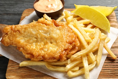 Photo of British traditional fish and potato chips on wooden board, closeup