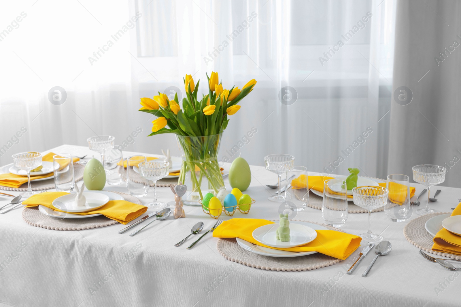 Photo of Festive table setting with glasses, painted eggs and vase of tulips. Easter celebration