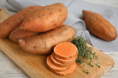 Wooden board with thyme and sweet potatoes on table, closeup