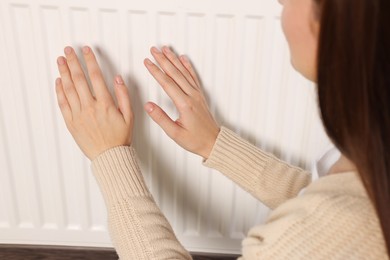 Photo of Woman warming hands on white heating radiator, closeup