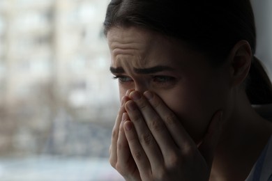 Photo of Sad young woman crying near window indoors, closeup with space for text. Loneliness concept