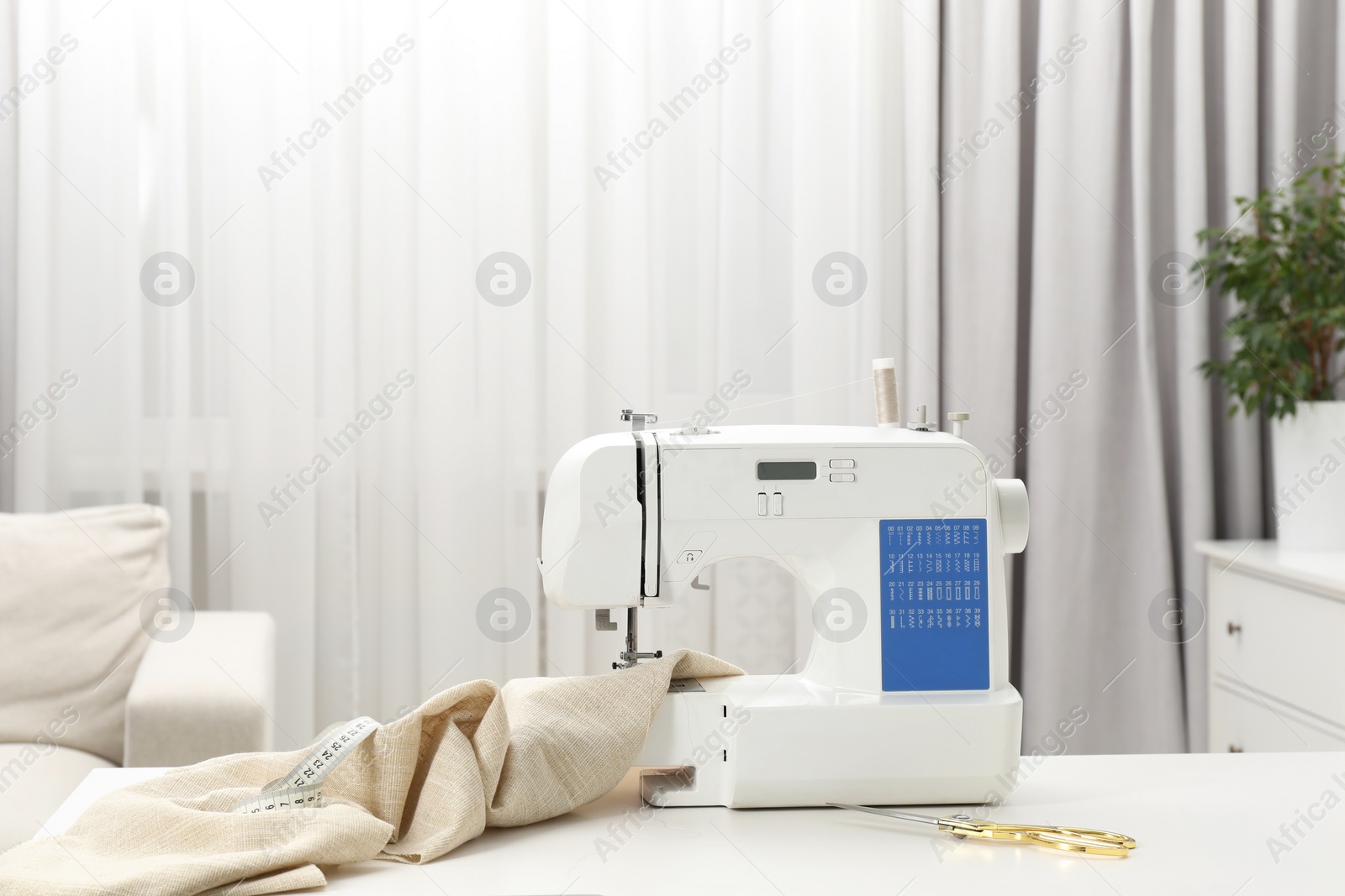 Photo of Sewing machine, measuring tape, scissors and fabric on white table in workshop