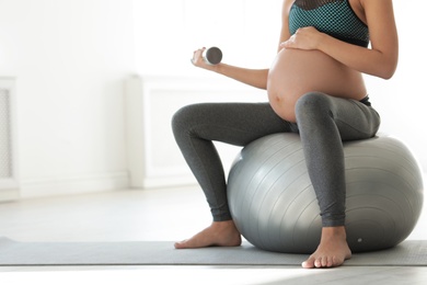 Photo of Young pregnant woman in fitness clothes lifting dumbbell at home, closeup. Space for text