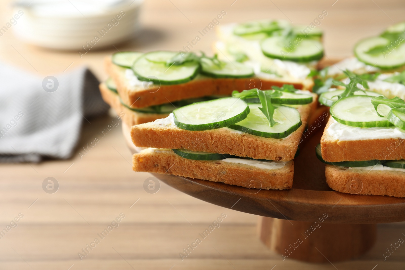 Photo of Wooden stand with traditional English cucumber sandwiches on table, closeup