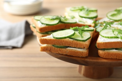 Photo of Wooden stand with traditional English cucumber sandwiches on table, closeup