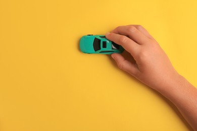 Photo of Child playing with toy car on yellow background, top view. Space for text