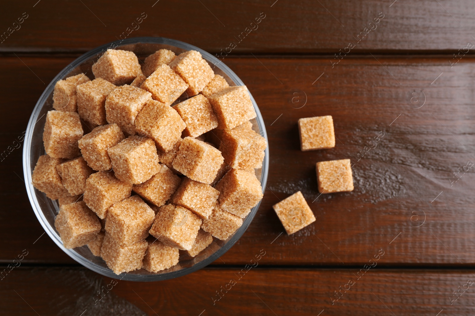 Photo of Brown sugar cubes in glass bowl on wooden table, top view