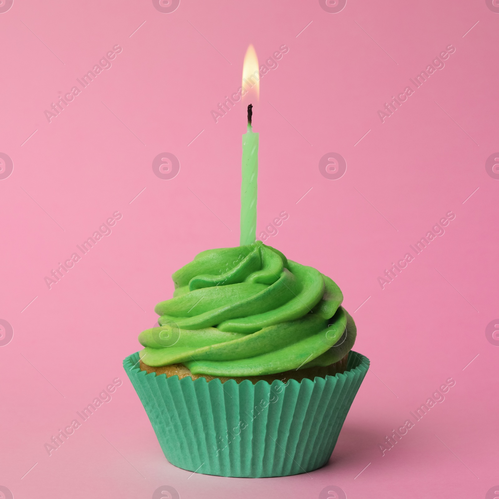 Photo of Delicious birthday cupcake with green cream and burning burning candle on pink background