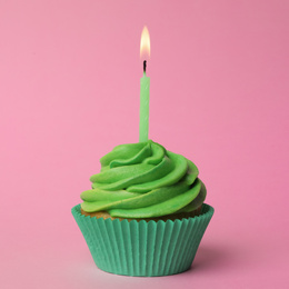 Delicious birthday cupcake with green cream and burning burning candle on pink background