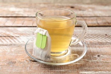 Photo of Tea bag in glass cup on wooden table, closeup