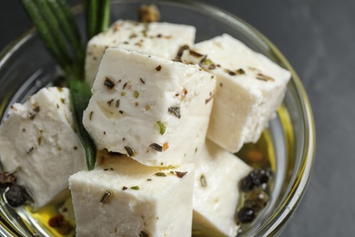 Photo of Pickled feta cheese in bowl on dark grey table, closeup