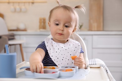 Photo of Cute little baby eating food in high chair at kitchen