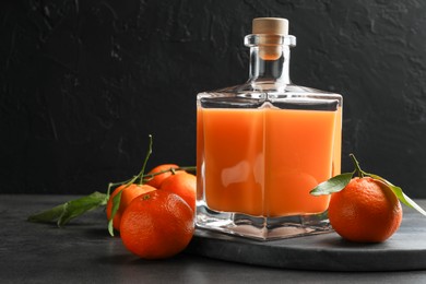 Photo of Delicious tangerine liqueur in glass bottle and fresh fruits on grey table, space for text