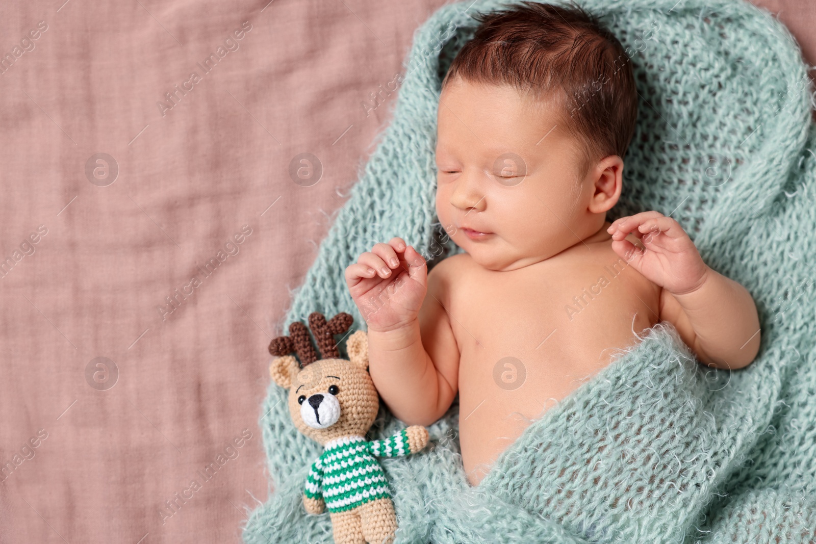 Photo of Cute newborn baby with toy deer in turquoise blanket sleeping on bed, top view. Space for text