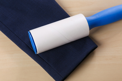 Lint roller and sleeve of jacket on wooden table, closeup