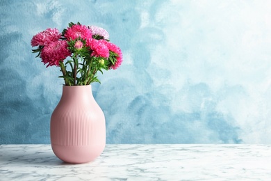 Vase with beautiful aster flower bouquet on table against color background. Space for text