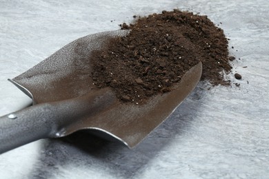 Photo of Metal shovel with fertile soil on gray textured surface, closeup