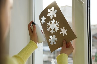 Photo of Woman using snow spray for decorating window with snowflakes at home, closeup