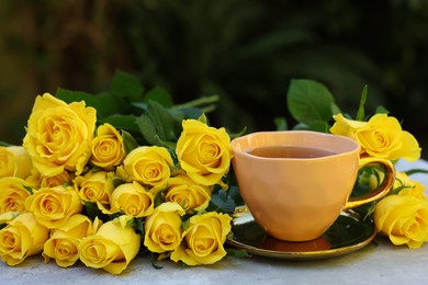 Photo of Cup of drink and beautiful yellow roses on light table outdoors