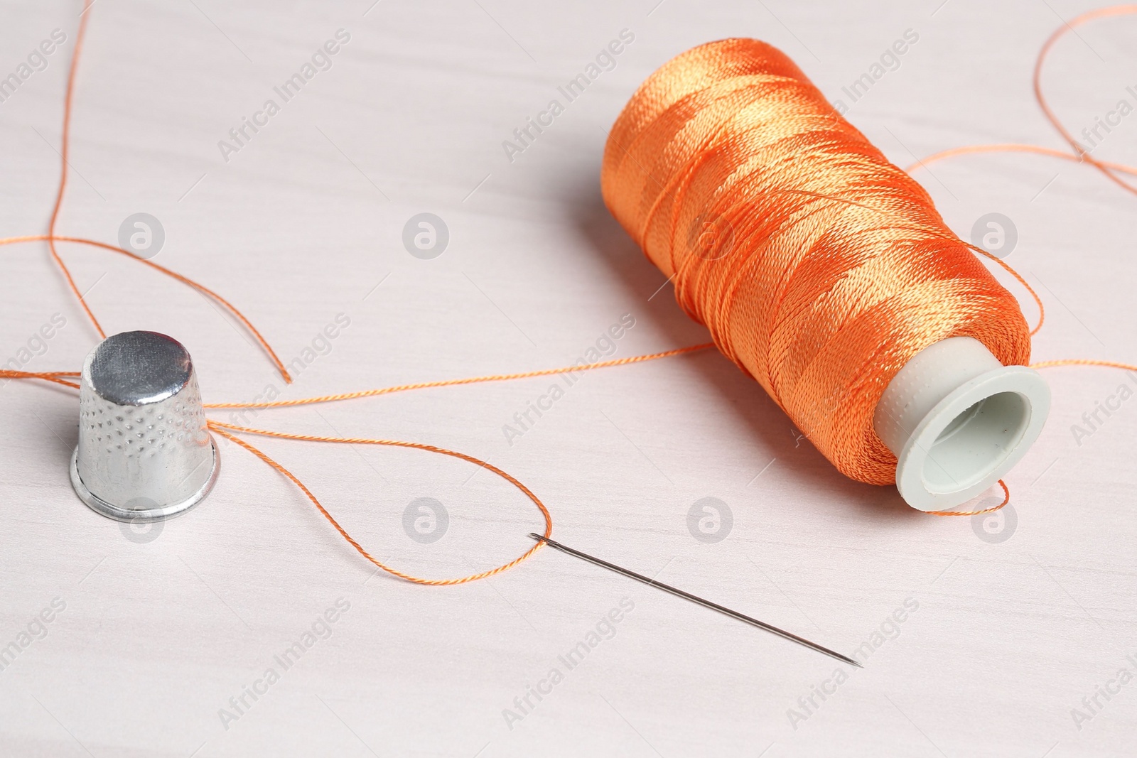 Photo of Sewing needle, spool of threads and thimble at light wooden table , closeup