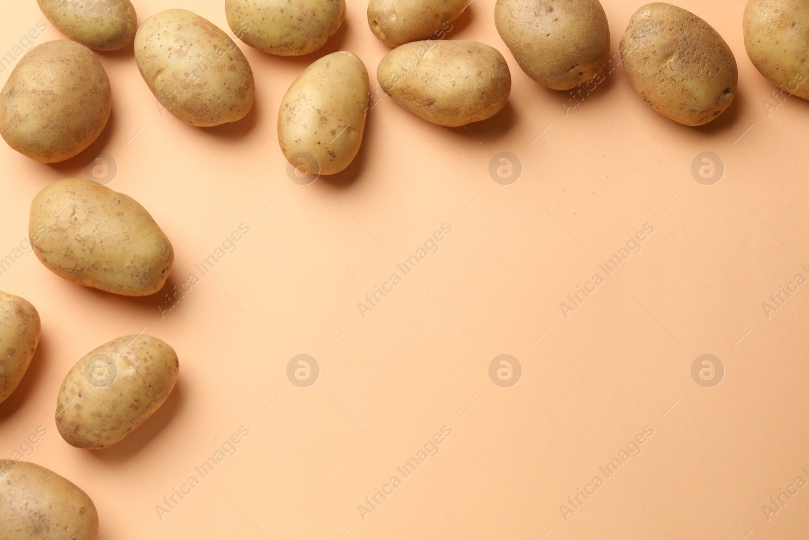 Photo of Fresh raw potatoes on pale orange background, flat lay. Space for text