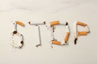 Photo of Word Stop made with burnt cigarettes on white marble table, flat lay. No smoking concept
