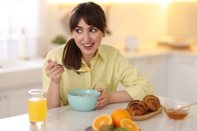 Photo of Smiling woman eating tasty cornflakes at breakfast indoors