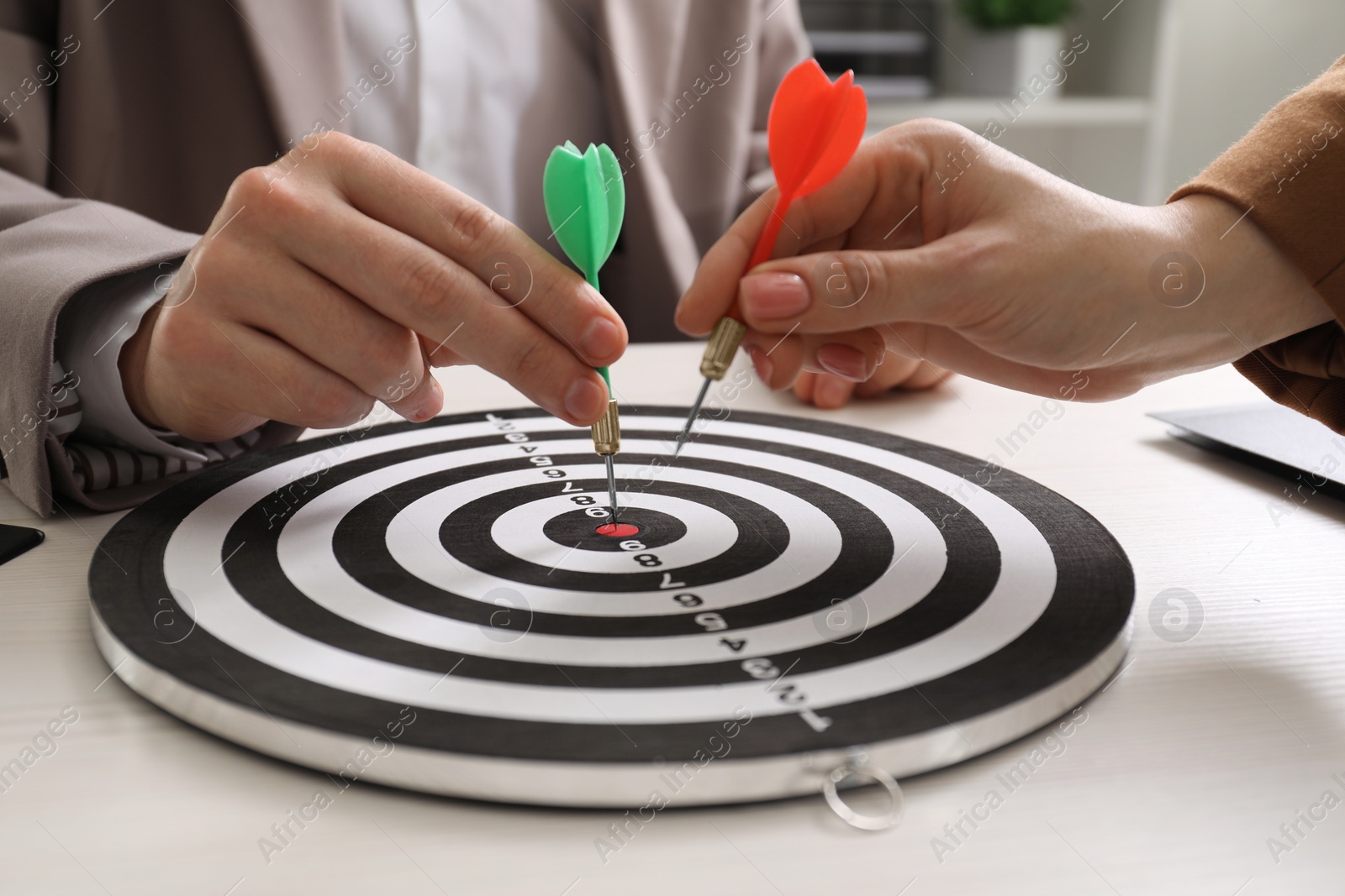 Photo of Business targeting concept. Man and woman with darts aiming at dartboard at white table indoors, closeup
