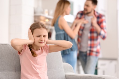 Photo of Little unhappy girl sitting on sofa while parents arguing at home