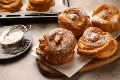 Many delicious profiteroles with powdered sugar on grey table