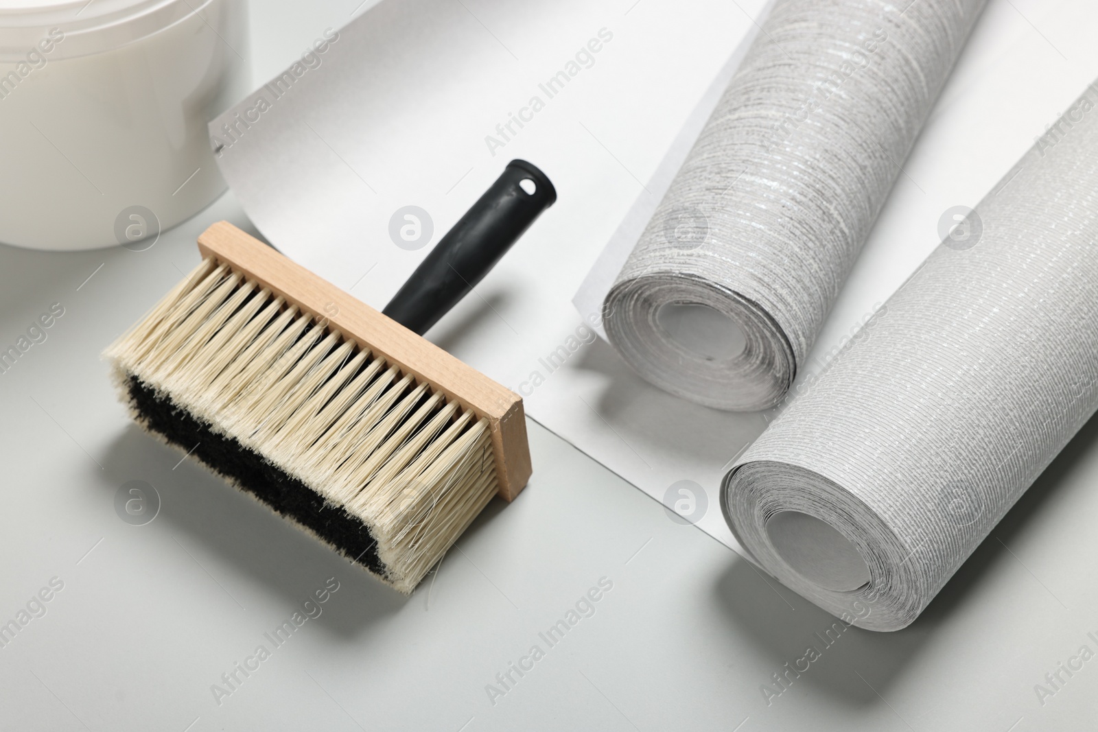 Photo of Different wallpaper rolls and brush on light grey background