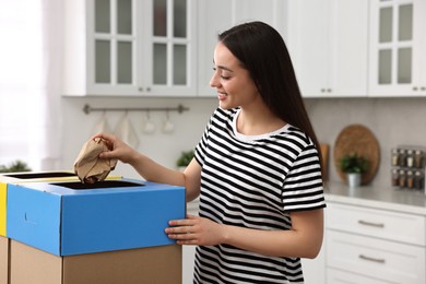Garbage sorting. Smiling woman throwing crumpled paper into cardboard box in kitchen