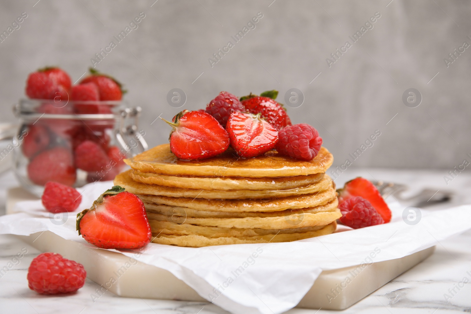 Photo of Tasty pancakes with fresh berries and honey on white marble table