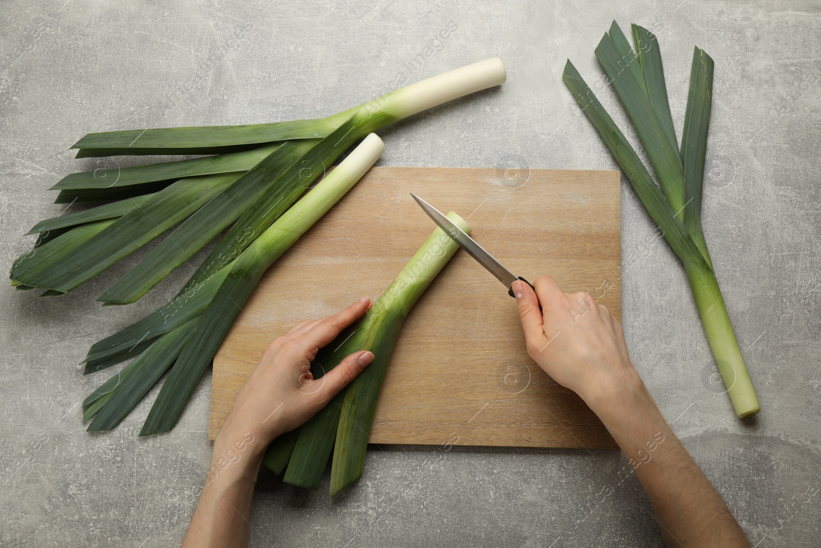 Photo of Woman cutting fresh raw leek at grey table, top view