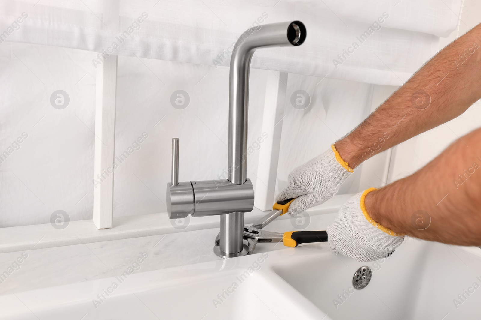 Photo of Man repairing water tap with wrench in kitchen, closeup